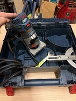 Bosch Colt palm router placed inside its plastic carrying case showing router, power cord, fence and wrench.