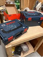 Two Bosch stackable carry cases closed on a wooden table, showing exterior condition and size difference.