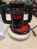 Front view of black Sears Craftsman buffer polisher with dual handles and attached white buffing pad on red base.