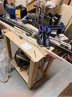 Photo showing two pairs of cross country skis, ski poles, ski boots placed on a wooden table in a storage setting.