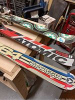 Side view of three pairs of skis showing the branded tops sheets and lengths: Dynastar 165, Atomic 158, Roxy 154.