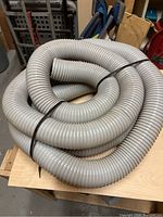 Three coiled grey flexible dust collection hoses, tied with black plastic straps, placed on a wooden table in a workshop environment.