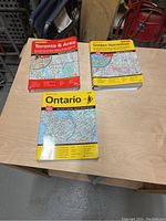 Three street atlases arranged on table, labeled Ontario, Toronto & Area, and Golden Horseshoe, showing front covers and map detail for Ontario atlas.