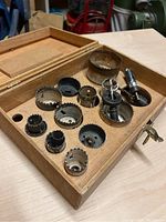 Open wooden carry case showing multiple hole saw cutters and mandrels arranged inside.