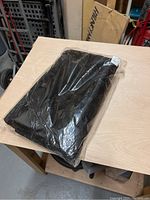 Full view of black insect netting folded inside clear plastic packaging on a wooden surface.