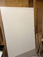 Photo showing one large rectangular white melamine board, approximately 49 x 72 inches in size, propped vertically inside a workshop space.