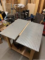 Two metal peg boards side by side on a wooden table in a workshop setting, displaying their size and hole pattern for organizing tools.