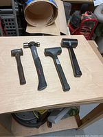 Four hammers placed on a wooden surface, showing different types and conditions, along with a leather tool top needing repair.