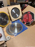 Box containing multiple saw blades including a dado cutting disc set in a red case, various other saw blades, and stabilizer washers.