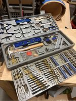 Open multi part tool kit plastic case showing various hand tools, drill bits, screwdriver bits, and hardware components.