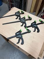Four Qwik brand clamps: two of 12-inch length and two of 6-inch length, all with black bars and green accents, on a wooden workbench.