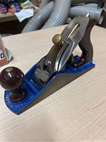Record smoothing hand plane showing blue metal body, maroon handle, brass adjustment knob, and polished steel blade with Record branding.