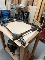 Adjustable rolling machine base on wooden workbench, showing metal frame with caster wheels and adjustable holes.