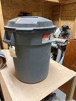 Gray medium-sized Rubbermaid garbage can with lid on wooden surface showing overall shape and condition.