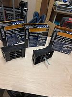 Two black plastic Stinson saw horse brackets on a table with boxes in the background