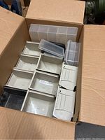 Box containing multiple Akro USA plastic shop organizing bins in beige and clear colors, with various compartment configurations and removable lids, some need cleaning.