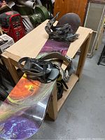Full view of the snowboard with attached black bindings, placed on a wooden table in a workshop or garage setting.