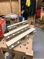 Three identical tip out storage bin units placed on a wooden workbench, showing the front with clear tip out drawers labeled with white stickers.