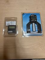 Two Wixey digital measuring tools in packaging on a wooden surface. One is a compact digital angle gauge with a digital display. The second is a larger U-shaped tool with a digital display and a precision scale for measurements and machine setup.