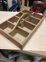 Wooden screw and nail carry organizer with eight compartments and a central handle, made from solid wood, shown from a side angle on a light wood surface.