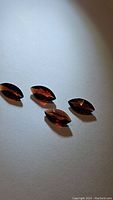 Four faceted marquise cut Amandine garnet gemstones on a white background under lighting, showing deep red orange color and clarity.