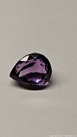 Close-up image of a pear cut Brazilian amethyst gemstone showing its facets and deep purple color.