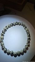 Photo of natural Dalmatian Jasper bracelet laid flat, showing cream colored beads with black spots on a white surface with dark surroundings