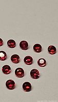 Top-down photo of 16 round-cut fire orange red sapphires scattered on a plain background showing color and clarity.