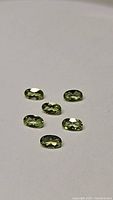 Six oval cut natural apple green peridot gemstones arranged on white background showing facets and clarity.
