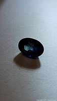 Oval cut natural blue sapphire gemstone displayed on a light surface with visible blue color tones and faceting details.