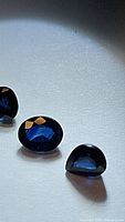 Close-up photo showing three natural blue faceted sapphires with deep rich blue color, displayed on a light surface with some shadowing.