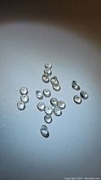 Photo showing multiple small, round, transparent white topaz stones arranged loosely on a light surface with good visibility of size and clarity.