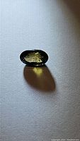 Oval cut champagne green tourmaline gemstone photographed on a white textured background showing color and faceting details.