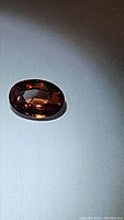 Oval cut natural fire orange zircon gemstone shown on a white background with focused lighting highlighting clarity and color.