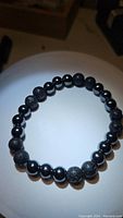 Photo showing the stretchy bracelet arranged in a circle with alternating textured lava stone beads and shiny hematite beads.