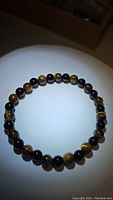 Photo of natural yellow Tigerseye and black Onyx bead stretchy bracelet on white background, showing circular form and bead details.