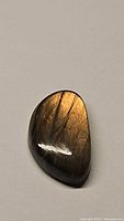 Close-up photo of the polished labradorite cabochon stone showing its orange flash and smooth surface.