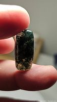 Translucent cushion-shaped natural moss agate cabochon held between fingers showing characteristic green moss-like inclusions and internal texture.