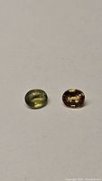 Two oval cut sapphire gemstones, one orange and one chartreuse, placed side by side on a white background.