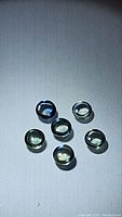 Six round cabochon teal blue sapphire stones laid out on a dark textured surface with slight reflections and shadows.