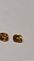 Close-up photo of two oval-shaped deep golden yellow sapphires side by side on a light background showing clarity and faceting.