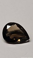Pear cut natural smokey quartz gemstone shown on a plain background, faceted with a dark smoky brown color.