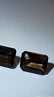 Pair of emerald cut natural smokey quartz gemstones with brownish-gray color shown on white background.