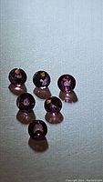 Six round cut pink-purple sapphires arranged on light surface showing clarity and color.