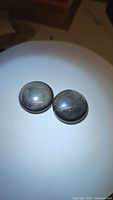 Pair of round polished cabochon silver sheen obsidian gemstones shown from a top angle under light, showing metallic sheen.