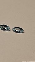 Two sky blue topaz gemstones in marquis cut placed on a neutral surface, showing their shape, color, and clarity.