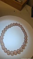 Top-down photo of strawberry quartz round bead bracelet laid in a circular shape on white surface with wooden box edge visible.