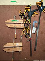 Photo showing set of Mastercraft clamps including two large wooden hand screw clamps, three black and yellow squeeze clamps, and one metal bar clamp.