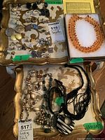 Wide shot showing two trays of assorted costume jewelry including earrings and necklaces along with one amber necklace in a box