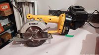 View of entire DeWalt DW936 cordless circular saw with battery attached and charger in background on white surface.